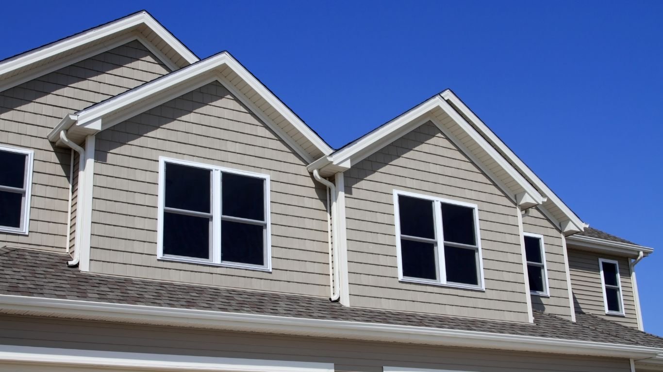 Close-up view of a beige house with multiple windows and a sloped roof, demonstrating quality siding services and craftsmanship.