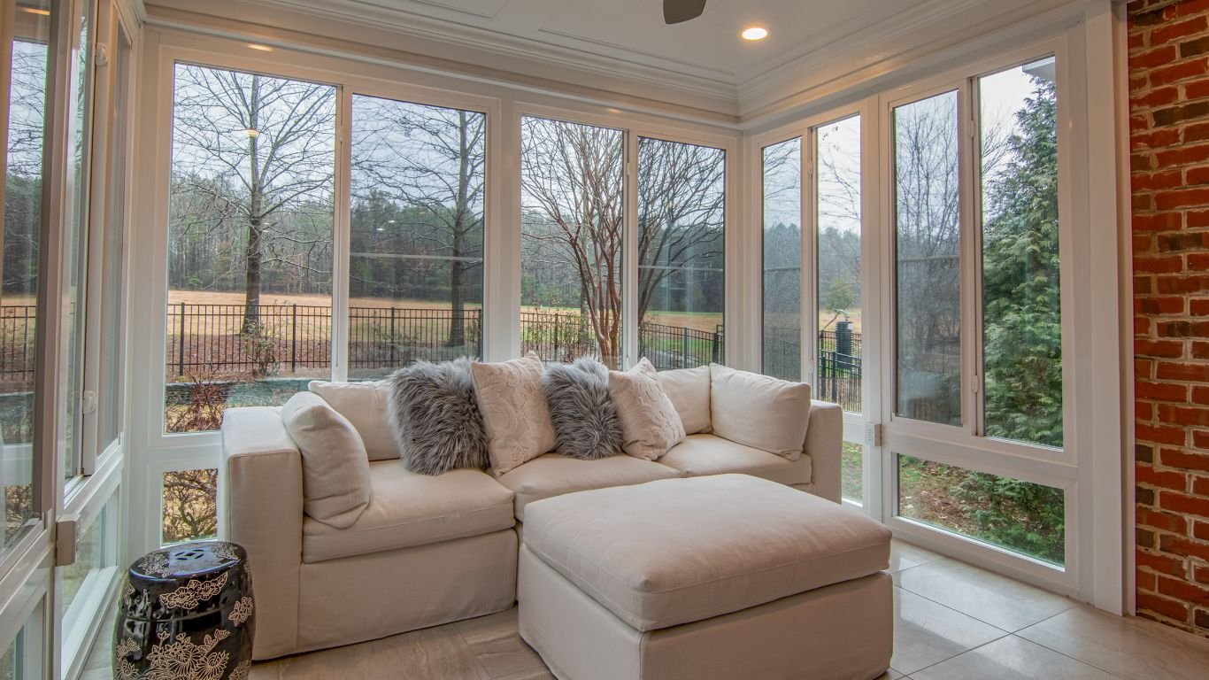 Cozy sunroom featuring a plush white sectional couch, large windows, and an inviting space for home remodeling and enhancements.