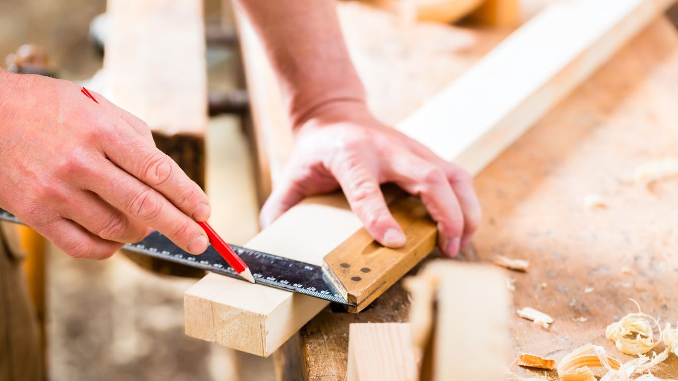 A carpenter measuring and marking wood with a square and pencil, showcasing custom carpentry skills for home remodeling.