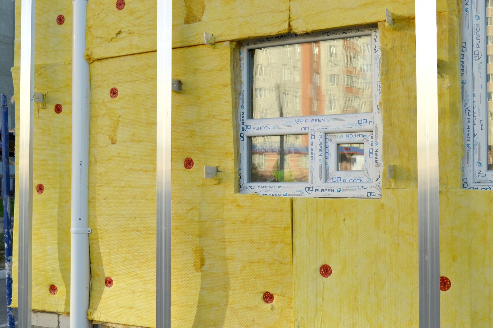 Close-up of a building under construction with yellow insulation panels installed on the exterior facade and aluminum framing. Duluth Construction specializes in professional siding installation and energy-efficient insulation solutions to enhance durability and thermal performance for homes and commercial properties.