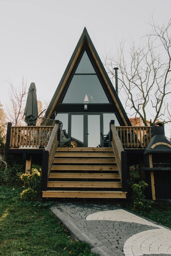 A modern A-frame cabin with a custom-built wooden staircase and deck, featuring sleek black trim and large glass windows. Duluth Construction specializes in deck and porch construction, framing, and exterior remodeling for stylish and functional outdoor spaces.