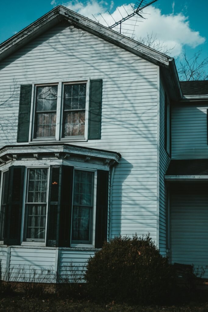 Older home with white siding, black shutters, and visible signs of wear. Duluth Construction specializes in siding repair, home restoration, and custom carpentry, ensuring durable and stylish exterior renovations.