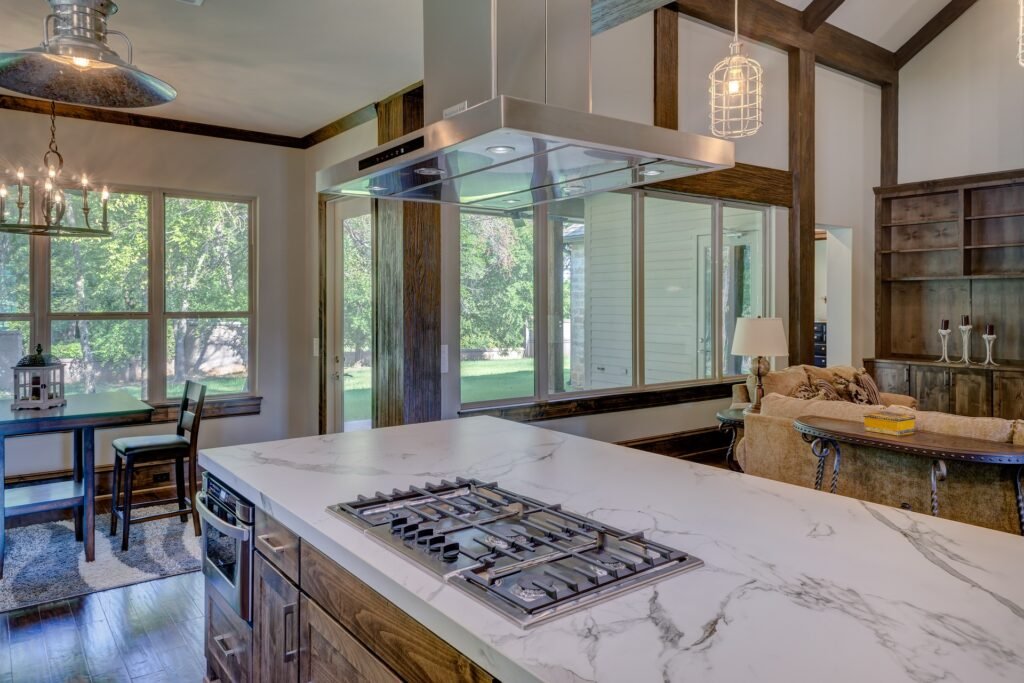 Modern open-concept kitchen designed by Duluth Construction, featuring a marble island with a built-in gas cooktop, wood cabinetry, and large windows.