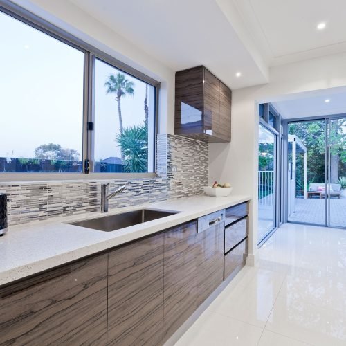 Modern kitchen with a sleek quartz countertop, stainless steel sink, and custom cabinetry by Duluth Construction, featuring a stylish backsplash.