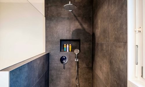 Modern walk-in shower renovation by Duluth Construction featuring dark custom tile work, a rainfall showerhead, built-in niche storage, and sleek fixtures.