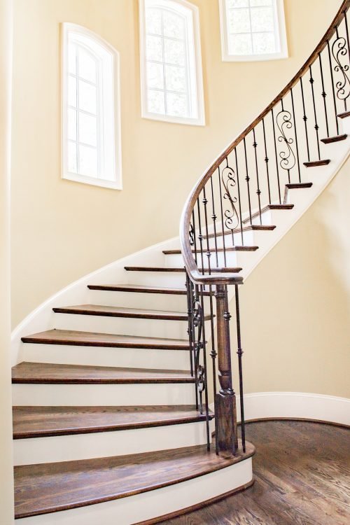 A grand curved staircase with dark wood steps and ornate wrought iron railings in a luxury home. Duluth Construction specializes in interior painting, custom finishes, and home remodeling to enhance elegance and functionality.