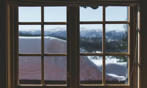 Rustic wooden-framed window with a snowy mountain view, featuring energy-efficient window installation by Duluth Construction.