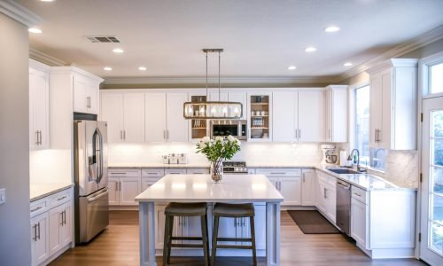 Bright modern kitchen with custom cabinet painting and refinishing, elegant lighting, and a spacious island. Duluth Construction provides expert interior painting and renovation services for a stylish and functional home.