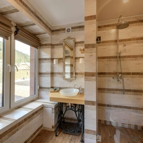 Rustic bathroom remodel by Duluth Construction featuring custom tile work, a vintage-style vanity, glass shower enclosure, and large windows for natural light.