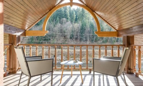 A beautifully crafted wooden balcony overlooking a scenic forest view, featuring intricate railing details and a cozy seating area. Duluth Construction specializes in deck and porch construction, custom carpentry, and high-quality exterior finishes.