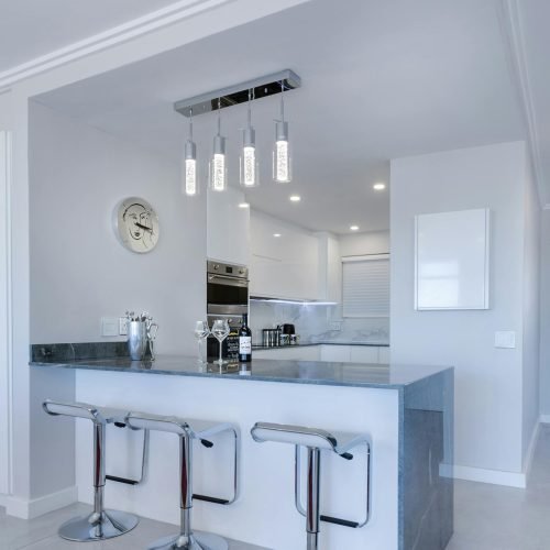 Modern white kitchen with a sleek marble countertop, stainless steel bar stools, and elegant pendant lighting. Duluth Construction specializes in high-end kitchen renovations, delivering stylish and functional designs.