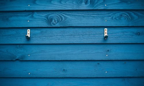 Close-up of vibrant blue wood siding with visible natural grain and metal hooks attached. Duluth Construction specializes in expert wood siding installation and repair, ensuring durability and aesthetic appeal for homes and businesses.