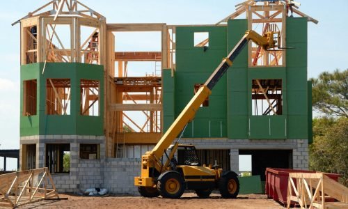 Home under construction with exposed wood framing, green sheathing, and a yellow telescopic handler. Duluth Construction specializes in framing near me, custom carpentry, and home remodelers for high-quality builds.