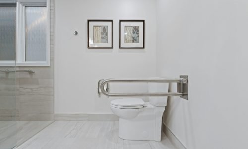 Accessible bathroom remodel by Duluth Construction featuring a modern toilet with a stainless steel grab bar, custom tile flooring, and a sleek glass shower.